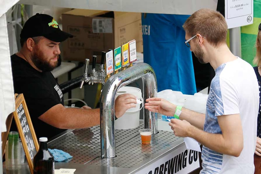 A man purchases a small beer sample from a bar tender.