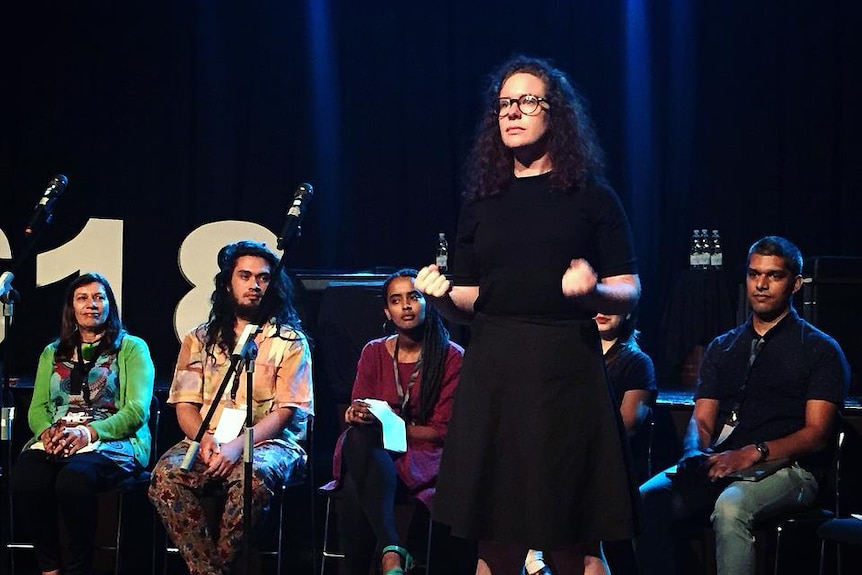 Fiona stands on a stage, with a row of people seated behind her.