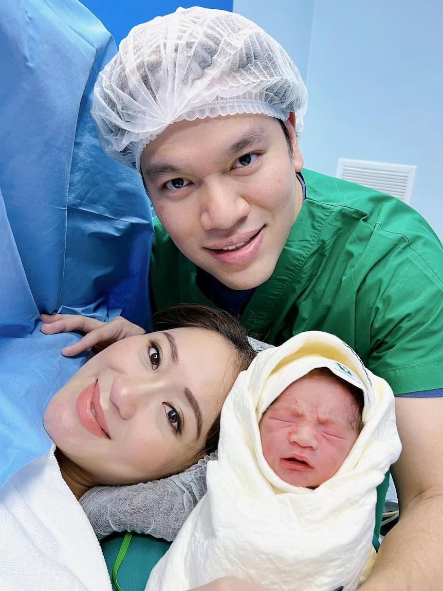 A couple pose for a photo with a newborn baby