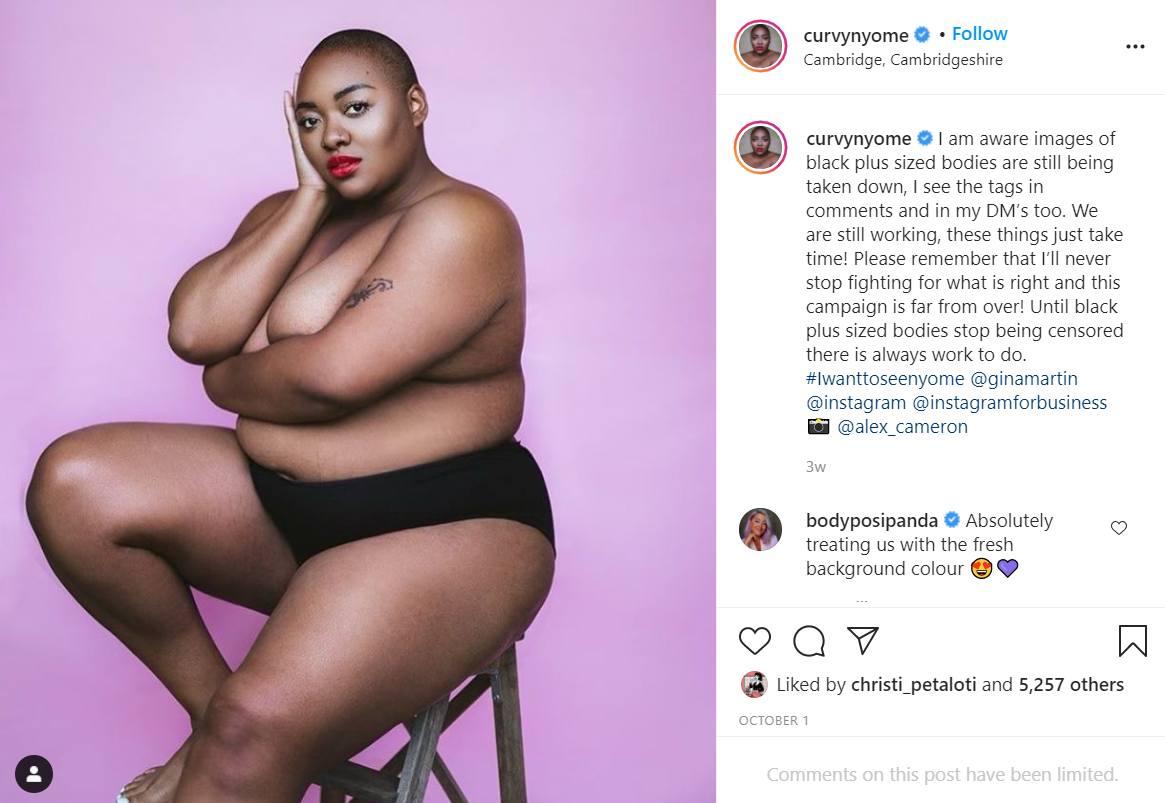 A screenshot of an Instagram photo with a bald black woman wearing only black underwear and covering her breasts.