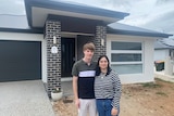 A young couple stand in front of a new house. 