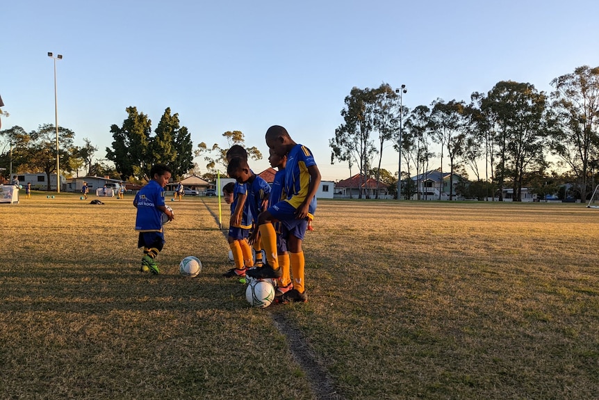 Some small boys line up with footballs.