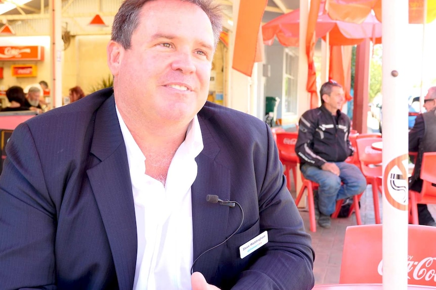 man in a blue jacket sitting at an outside table at a cafe