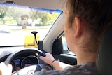 Lucy Haynes behind the wheel of a car with her learners permit in view.