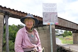 Woman stands in front of sign and railway bridge