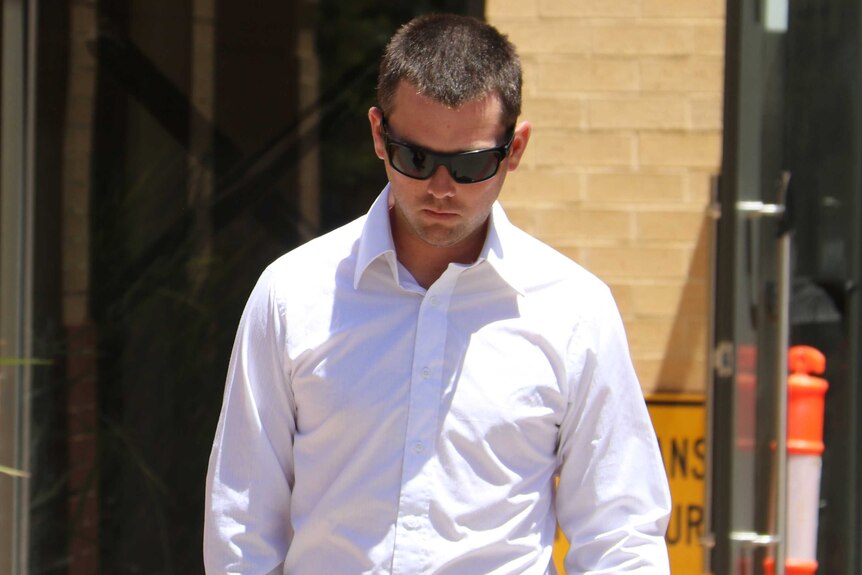 A man wearing a white collared shirt and sunglasses walks with his head bowed outside court.