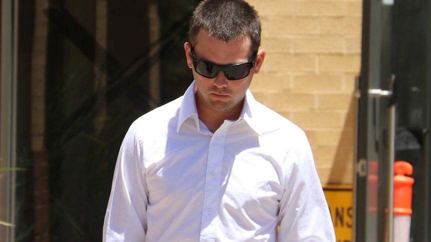 A man wearing a white collared shirt and sunglasses walks with his head bowed outside court.