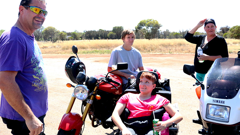 Shanniah Barker sits smiling in her wheelchair looking at her father David with mum Angela and brother Isaac in the background.