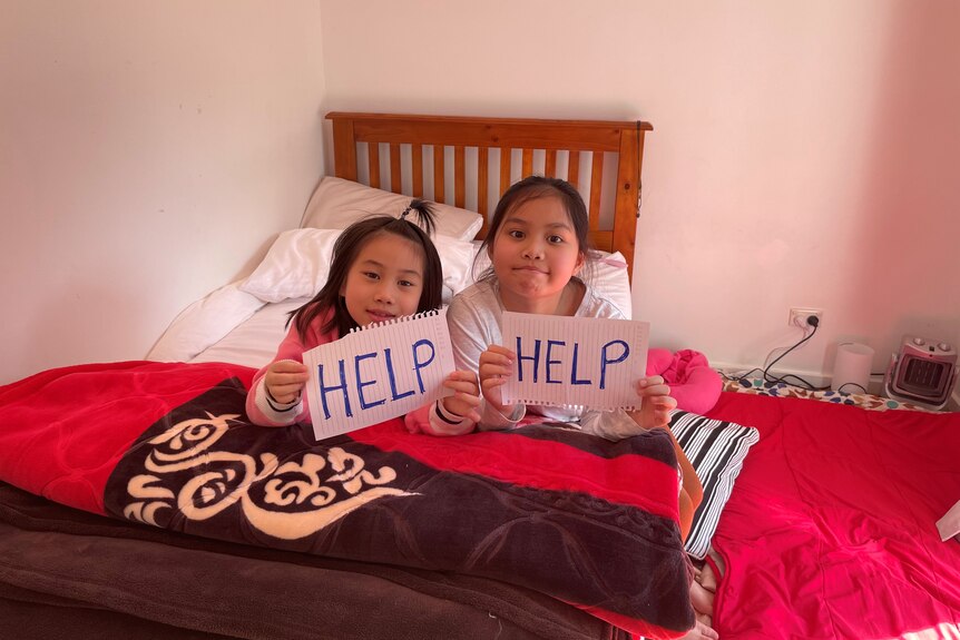 Two young girls on a bed with hand-written signs saying "HELP".