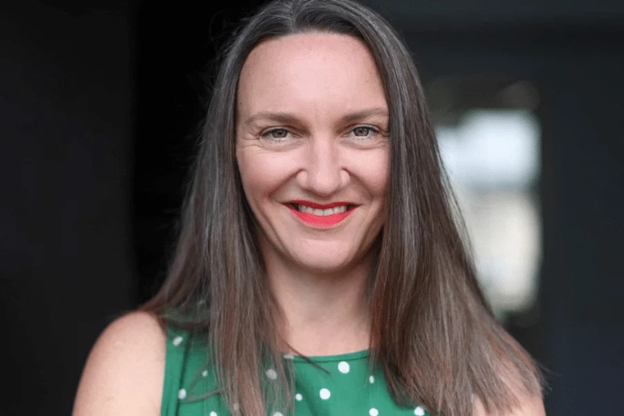 A headshot of Louise Stark, wearing a green dress, with a blurred background.