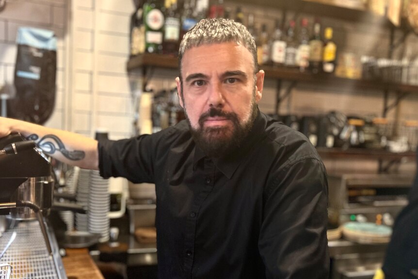 David Perrotta stands in front of the coffee machine in his cafe, dressed in black.