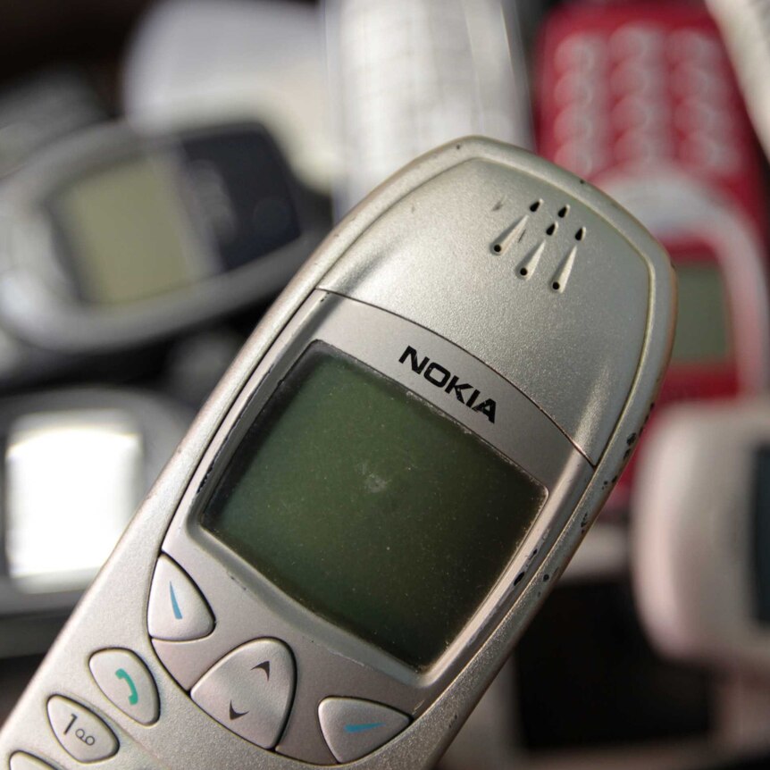 Several old model Nokia phones with black and white screens sit on a pile.