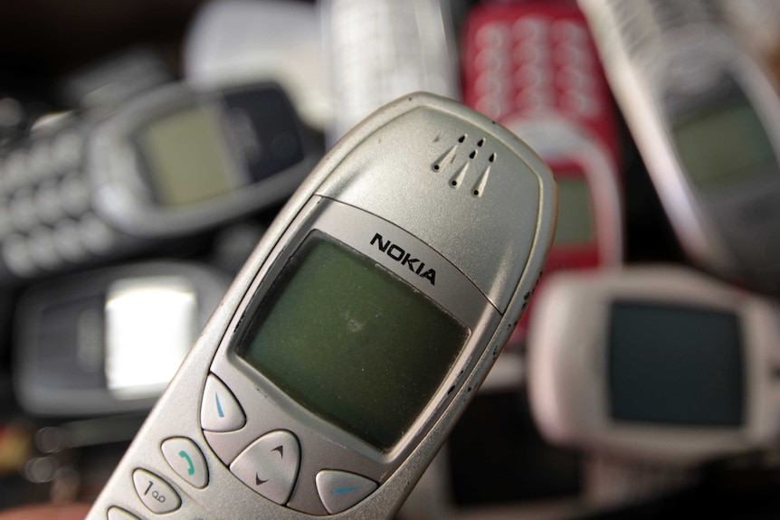 Several old model Nokia phones with black and white screens sit on a pile.