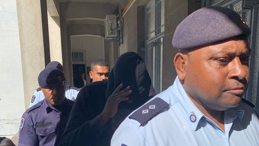 Henri Lusaka hides under his hoodie as police lead him into court