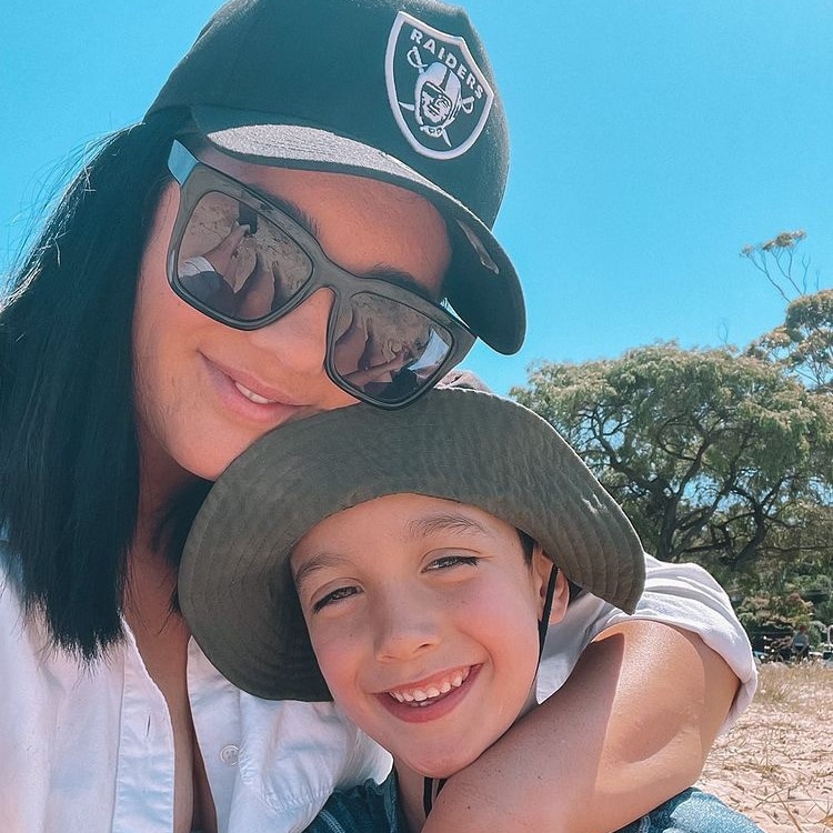 A woman in a black cap cuddles her primary school boy