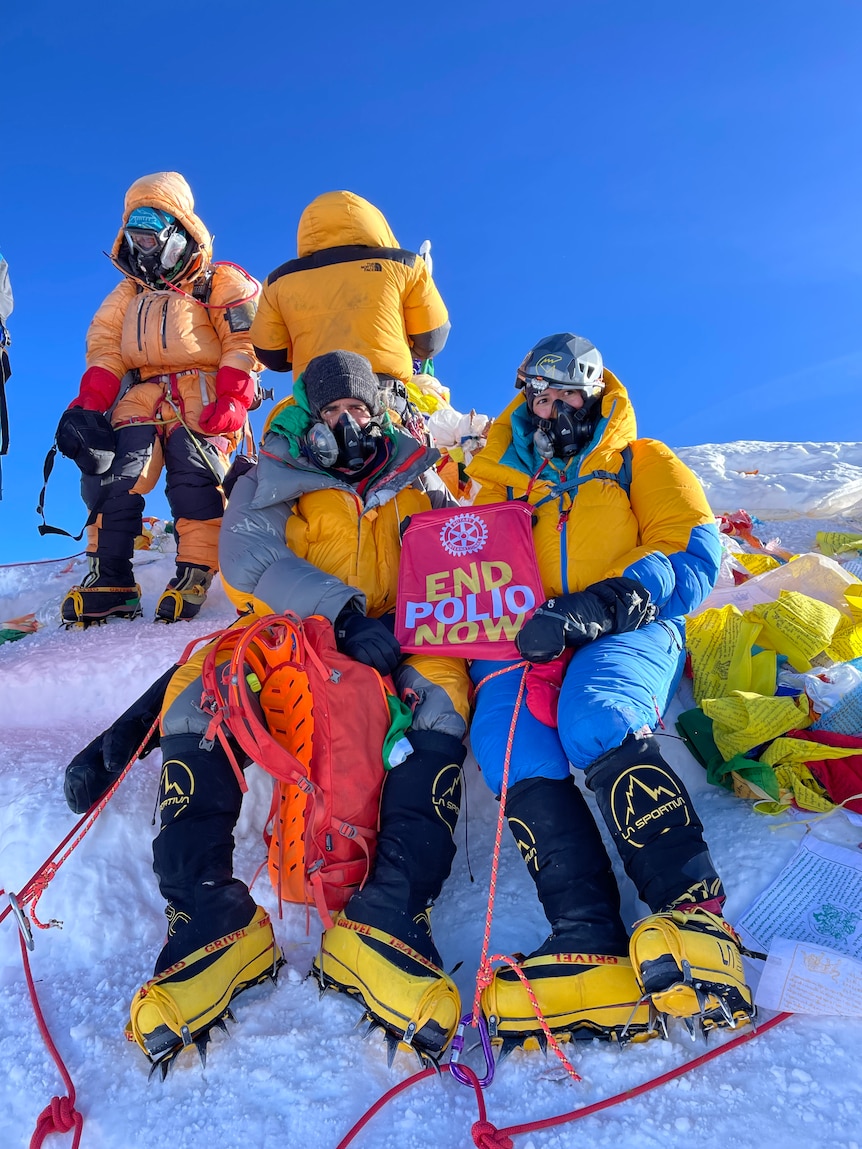 Two people hold a sign that says end polio now at the summit of the mountain. 