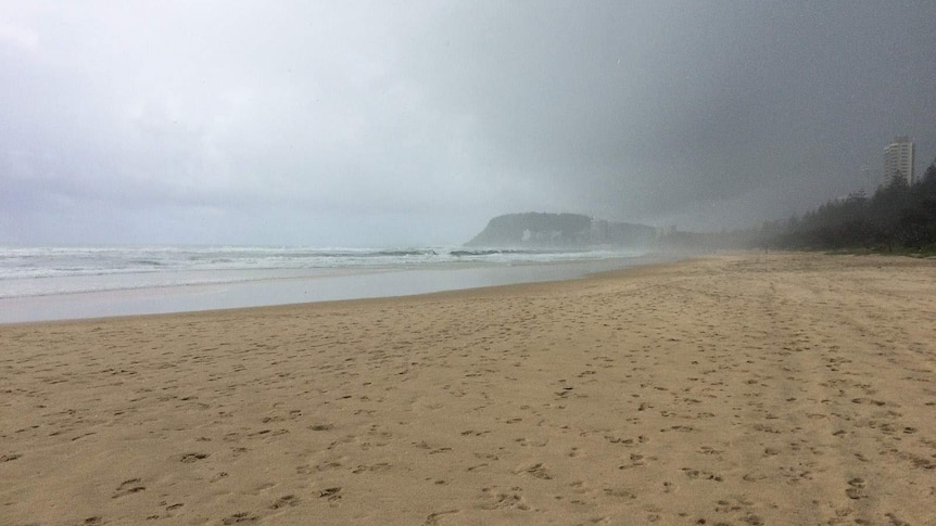 A Gold Coast beach shrouded in rain clouds, Burleigh headland in the distance