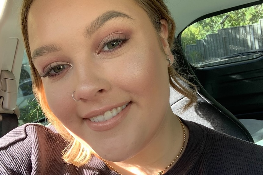 A close up of a woman smiling at the camera. She is wearing a black top and sitting in her car.