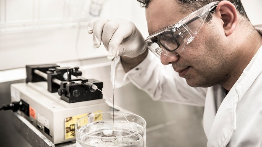A researcher in a laboratory pulling out synthetic yarn from a solution in a beaker