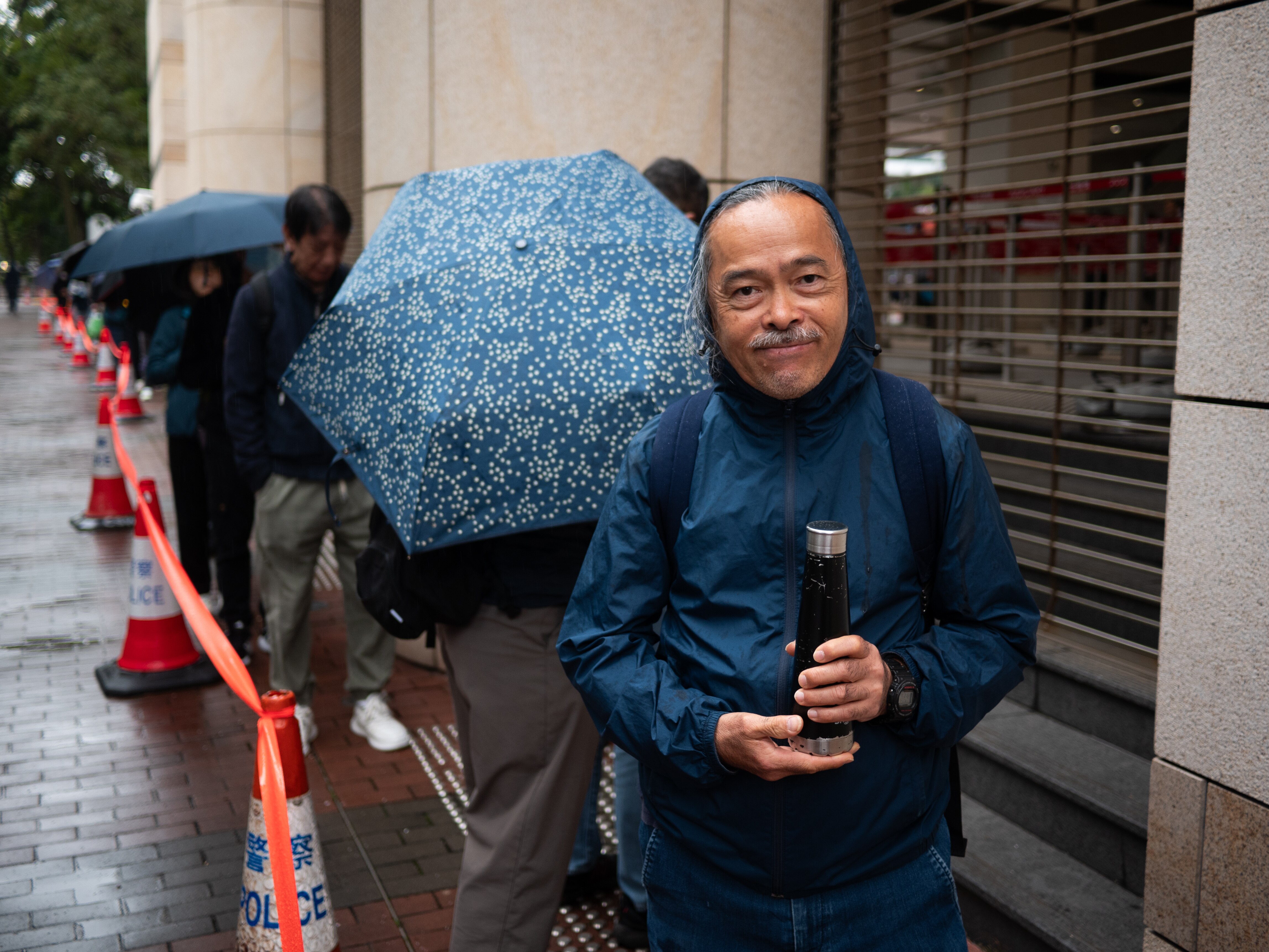 A man in a raincoat stands outside a court 