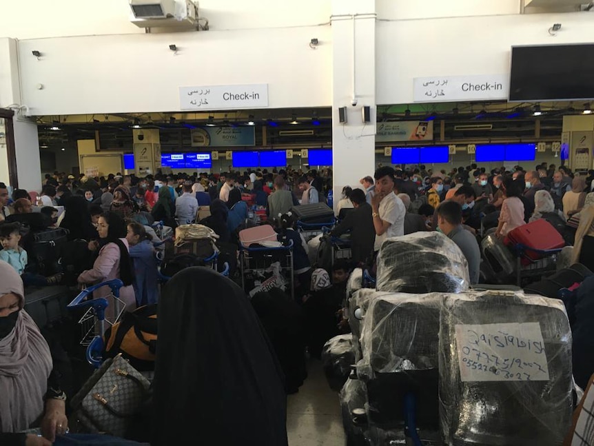Hundreds of people fill an airport terminal, lining up for check in counters.