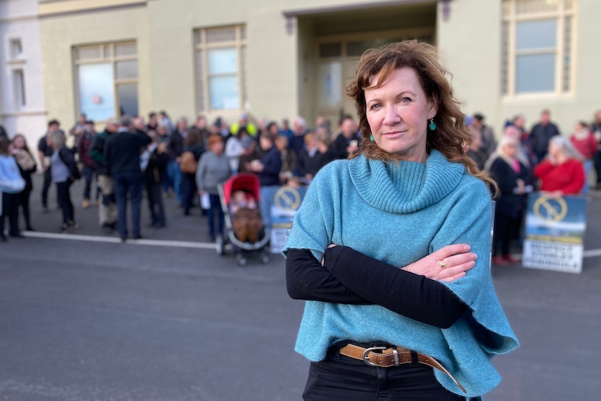 A woman with arms folded, with other people in the background.