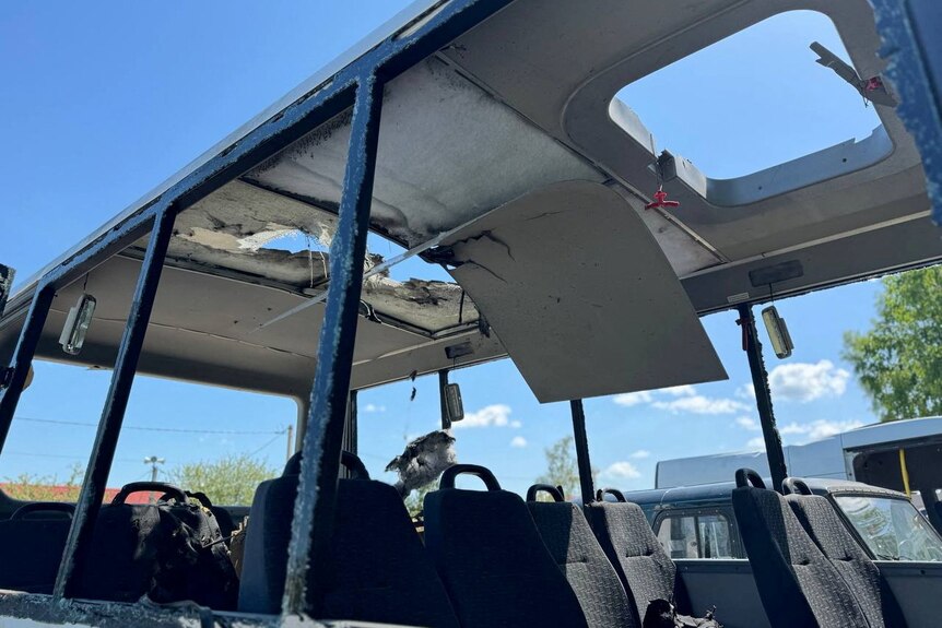 A bus with a hole in its roof and no windows sits in the open against a blue sky