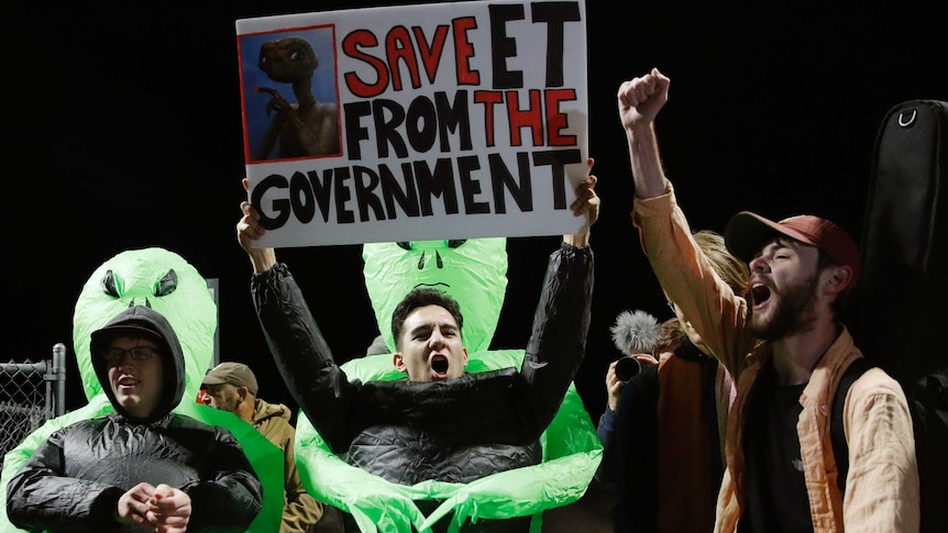 Area 51 party-goers wear alien costumes and hold signs defending ET