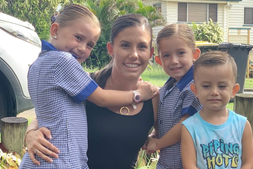 A mum hugs her three children in a driveway.