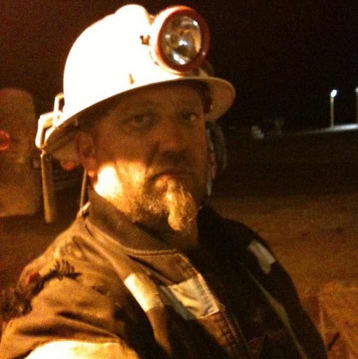 Shaun Southern takes a selfie in the dark wearing mining gear and a hard hat with a lamp on it.