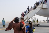 A family walks towards the staircase leading into a plane on a tarmac.