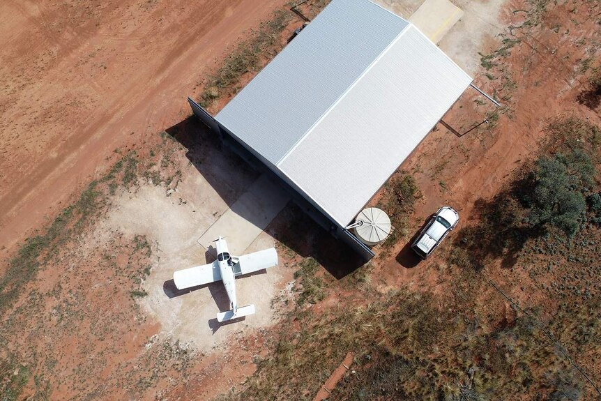 An aerial shot of a hangar with a plane in front of it, surrounded by red dirt.