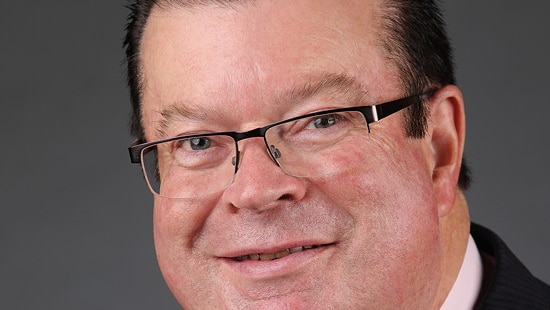 Bernie Finn smiles as he poses, in a suit and tie, wearing glasses.