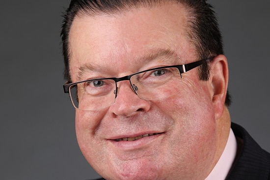 Bernie Finn smiles as he poses, in a suit and tie wearing glasses.