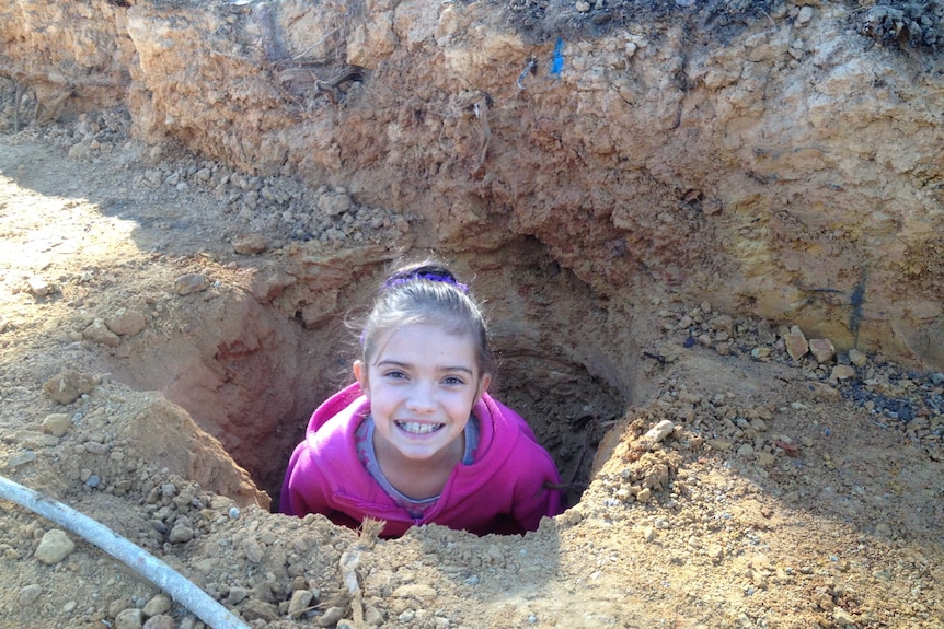 A young girl standing in a hole poking her head out