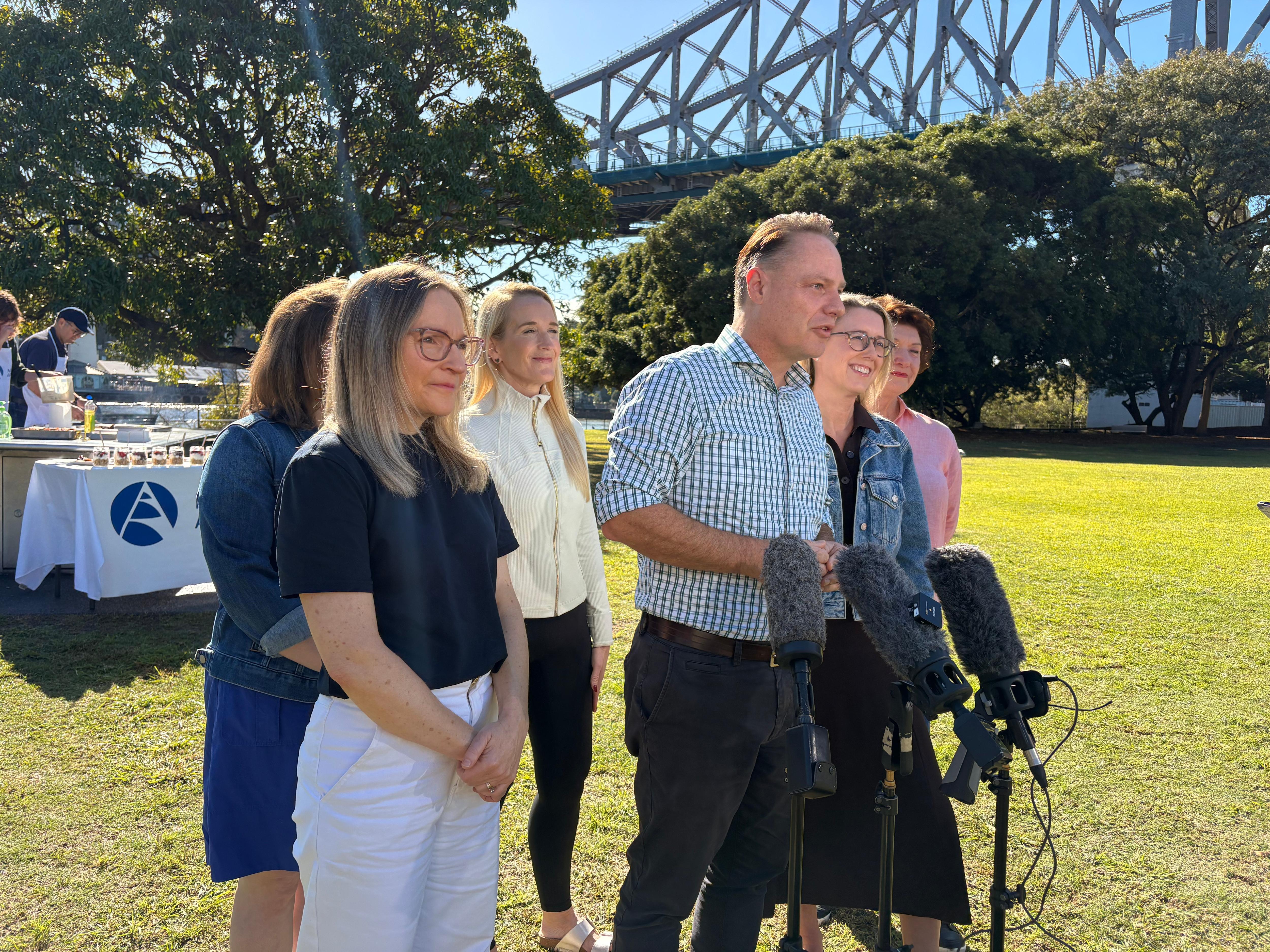 Adrian Schrinner speaking at press conference with Story Bridge in background.
