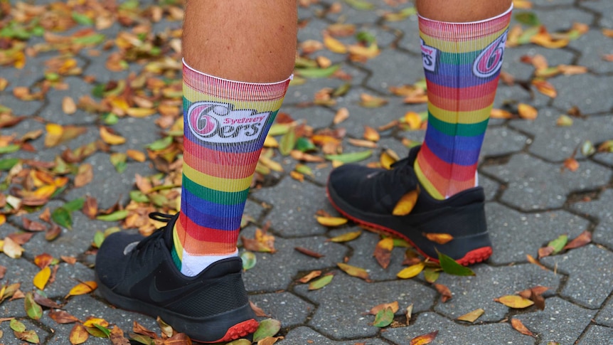 A man wearing rainbow socks of the cricket team Sydney Sixers stands in autumn leaves.