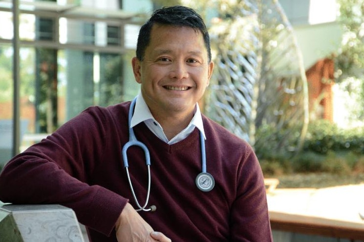 a man with a stethoscope around his neck sitting down and smiling
