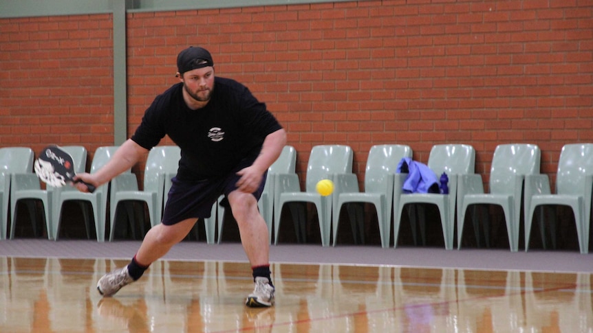 A man prepares to hit a yellow ball with a paddle while playing the game pickleball.