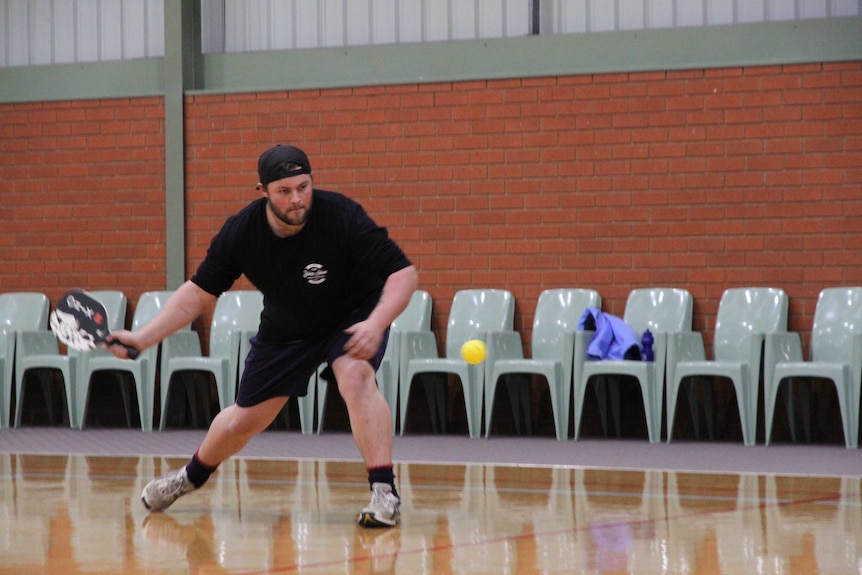 A man prepares to hit a yellow ball with a paddle while playing the game pickleball.