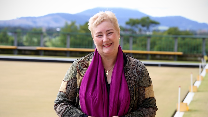 Ann Sudmalis stands at a bowling green with a mountain in the background.