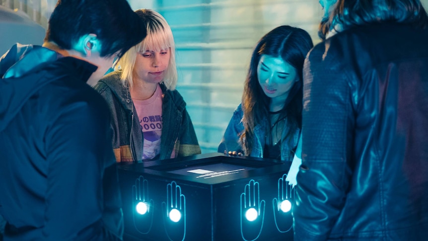 Four people stand around a video game installation looking down at the screen