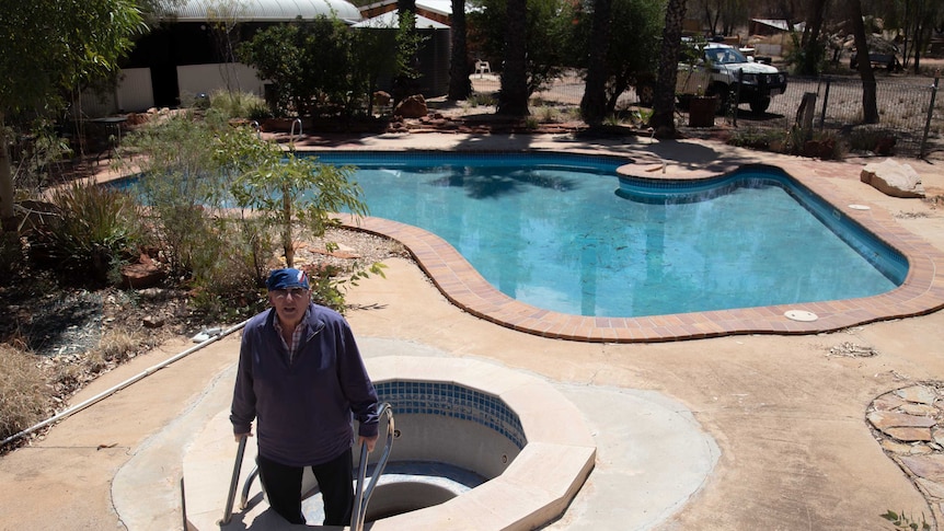 A man stands in an empty spa that sits next to an Australia-shaped pool, in the position where Tasmania would be.