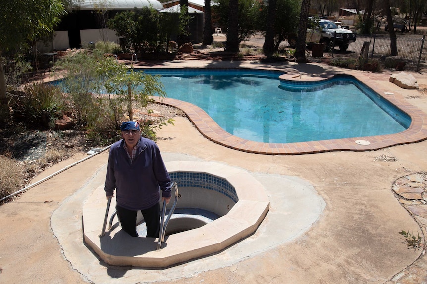 A man stands in an empty spa that sits next to an Australia-shaped pool, in the position where Tasmania would be.