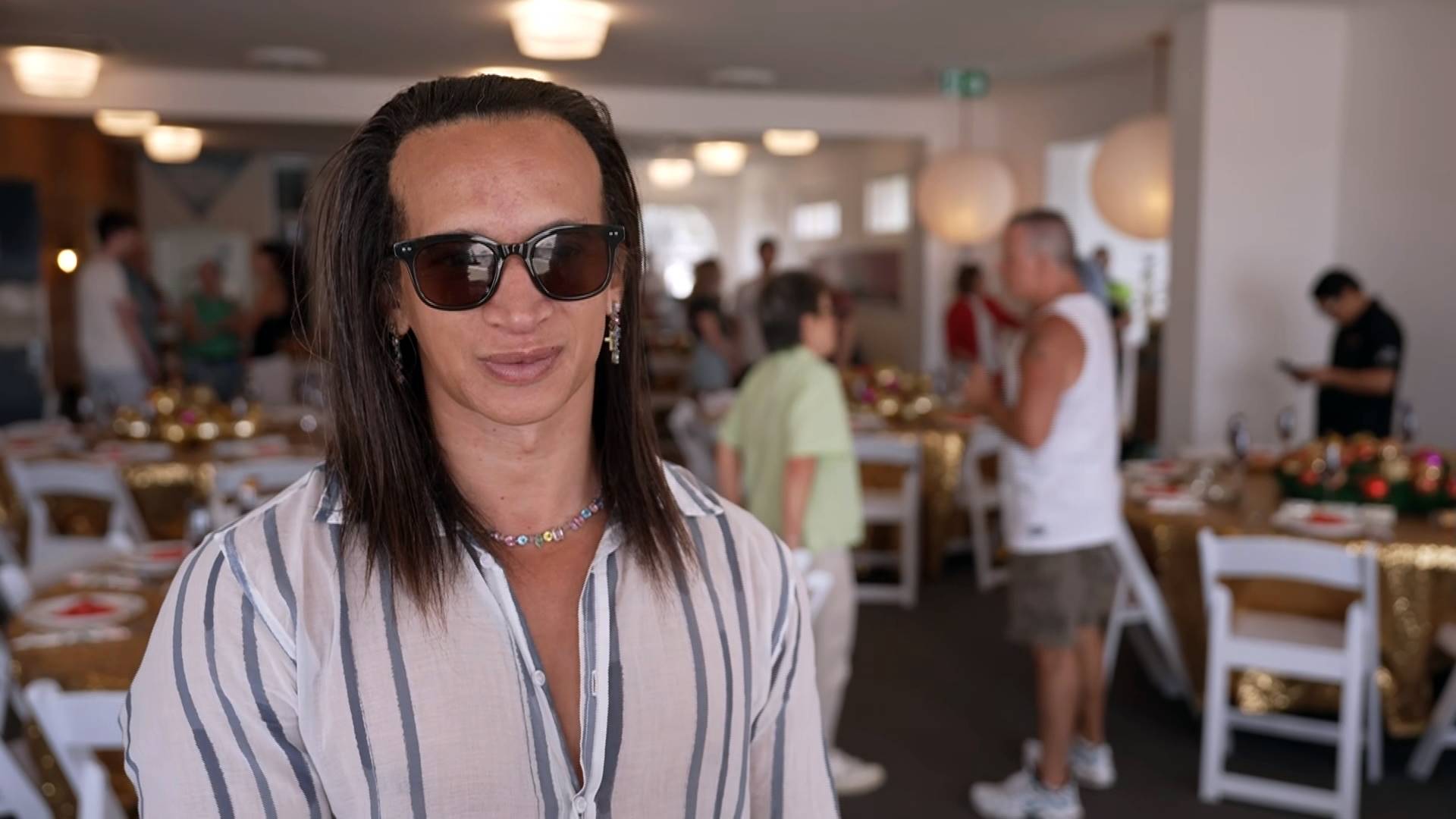 Sebastian Cassie, organizador do almoço na praia de Bondi para a comunidade, usa óculos escuros dentro de casa enquanto conversa com o medai.