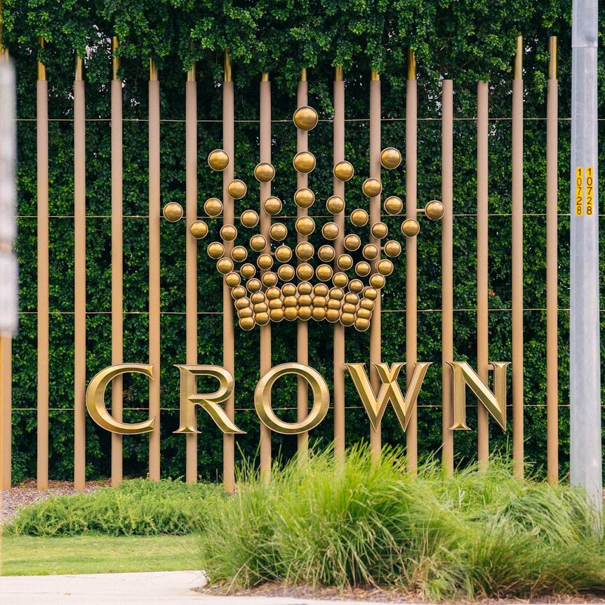 A sign showing the Crown Resorts logo in front of shrubs beside a road.