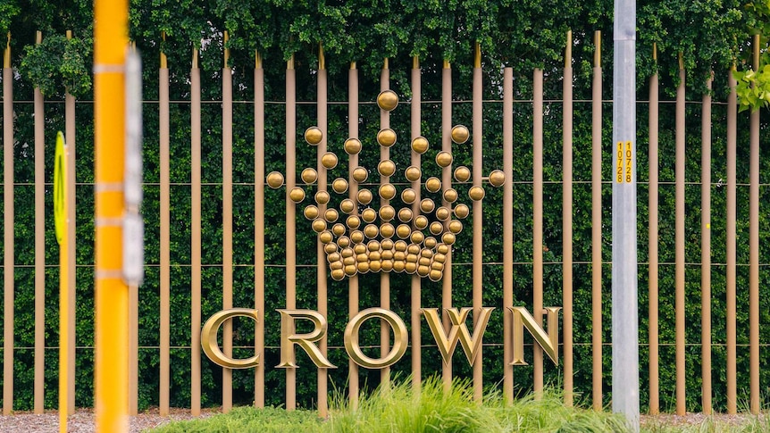 A sign showing the Crown Resorts logo in front of shrubs beside a road.