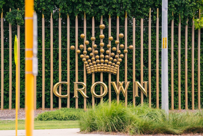 A sign showing the Crown Resorts logo in front of shrubs beside a road.