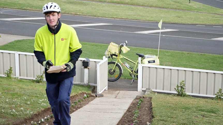 Postie Leon Craig walks up a footpath carrying a package.
