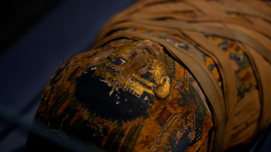 A closeup of the decorative, gold painted face covering on the mummified body of a boy 